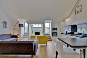 En moderne opholdsstue med sofa, gule lænestole, et spisebord og et køkken med hårde hvidevarer.