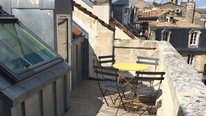 A rooftop terrace with a wooden deck, a yellow table, and black chairs.
