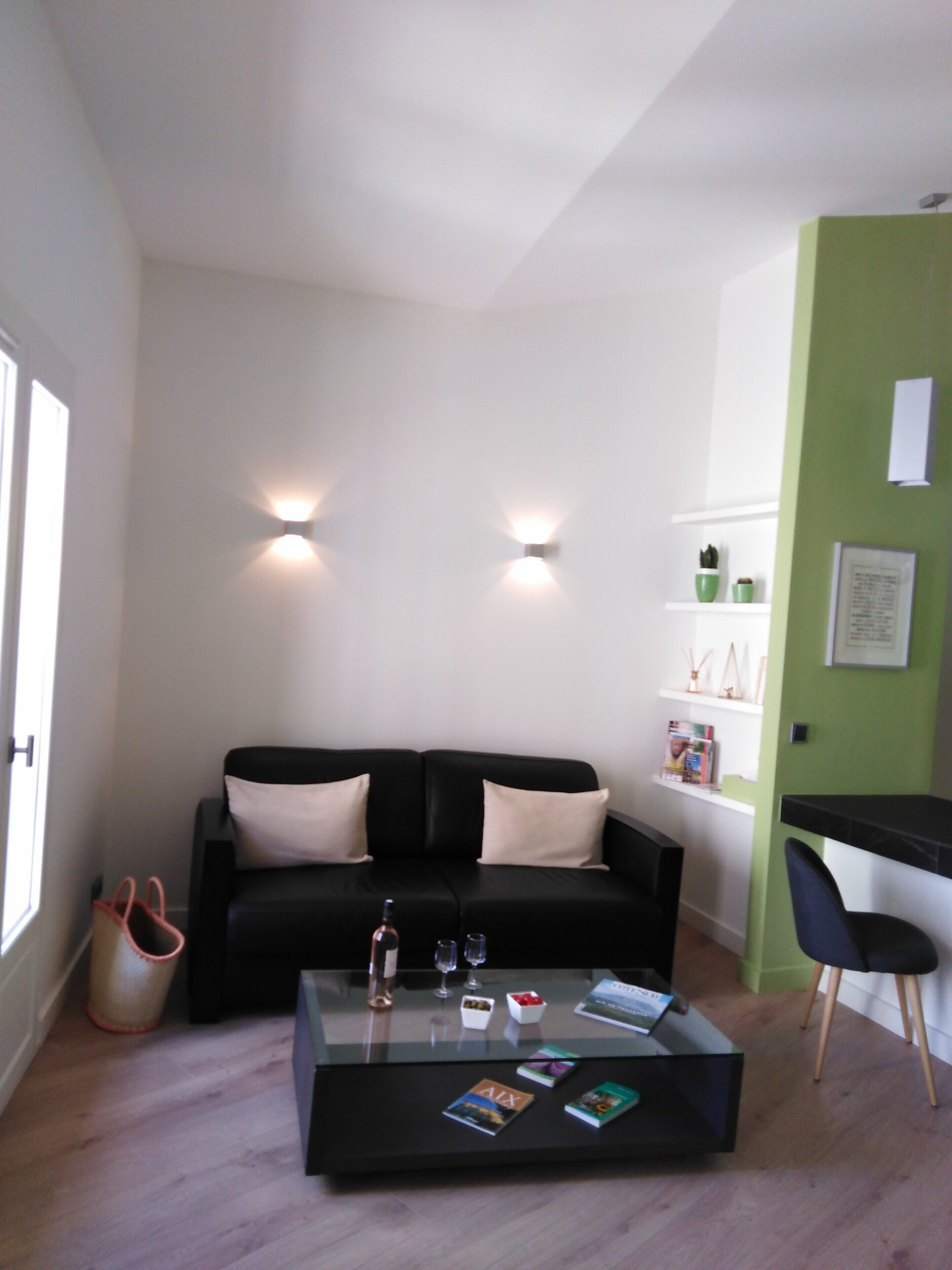 A modern living room with a black sofa, a glass coffee table, and a green accent wall.