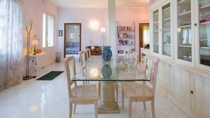 A dining area with a glass table surrounded by chairs, a vase, and a bookshelf. - B&B Villa il Glicine (Porto Mantovano)