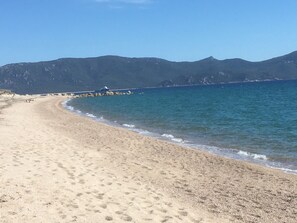 Une plage de sable fin aux vagues douces, une jetée qui s’avance dans l’eau et, au loin, des montagnes.