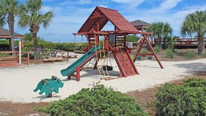 Ein Spielplatz mit Rutsche und Klettergerüsten, umgeben von Palmen und Picknicktischen.