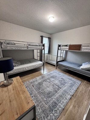 Un dormitorio con literas, un escritorio con lámpara, un tapete estampado y una ventana con cortinas.