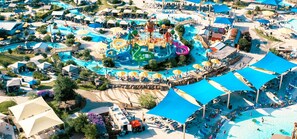 Vista aérea de un parque acuático con múltiples toboganes y piscinas, rodeado de zonas sombreadas y sillas de playa.