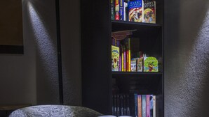 A chair with an open magazine, a bookshelf with various books, and a lamp in a room with a textured wall.