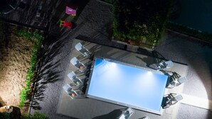 An aerial view of a rooftop terrace with a rectangular pool, surrounded by outdoor seating and greenery.