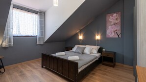 Une chambre avec un plafond en pente, un lit avec une literie à motifs, deux tables de chevet et un luminaire fixé au mur.