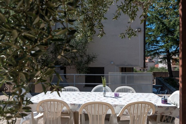 An outdoor dining area with a table and chairs, surrounded by foliage. - JASNA, 3-bedroom budget accommodation, 100m from a beach (Okrug Gornji)