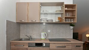 Une cuisine compacte avec des meubles en bois, un lave-vaisselle encastré et un plan de travail sur lequel se trouve une bouilloire.