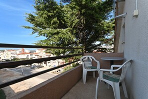 A balcony with two white plastic chairs and a small round table, overlooking a street with buildings and a tree. - JASNA, 3-bedroom budget accommodation, 100m from a beach (Okrug Gornji)