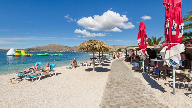 Une plage avec des transats, des parasols et un ciel bleu dégagé.