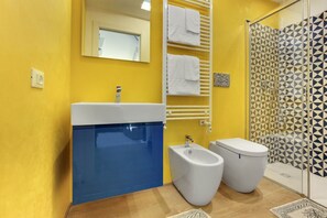 Un baño con pared amarilla, lavabo azul, un bidé, inodoro y ducha con azulejos de patrón geométrico.