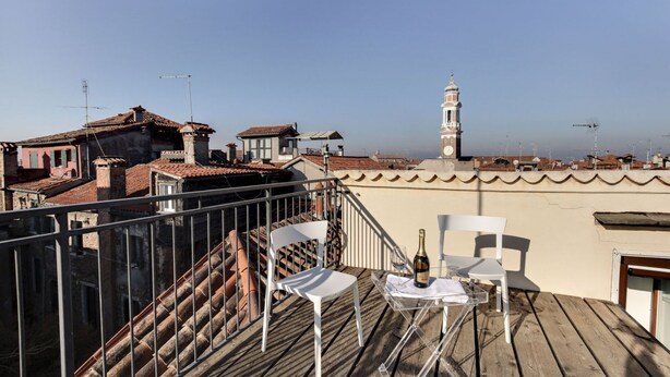 A rooftop terrace with a clear view of the city skyline, including a prominent tower. There are two white chairs and a small table with a bottle and glass. - VENICE SKYLINE VIEW STUDIO APARTMENT M0270429079 (Venice)