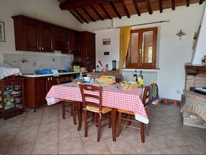 A kitchen with wooden cabinets, a dining table with a red and white checkered tablecloth, and a brick oven.