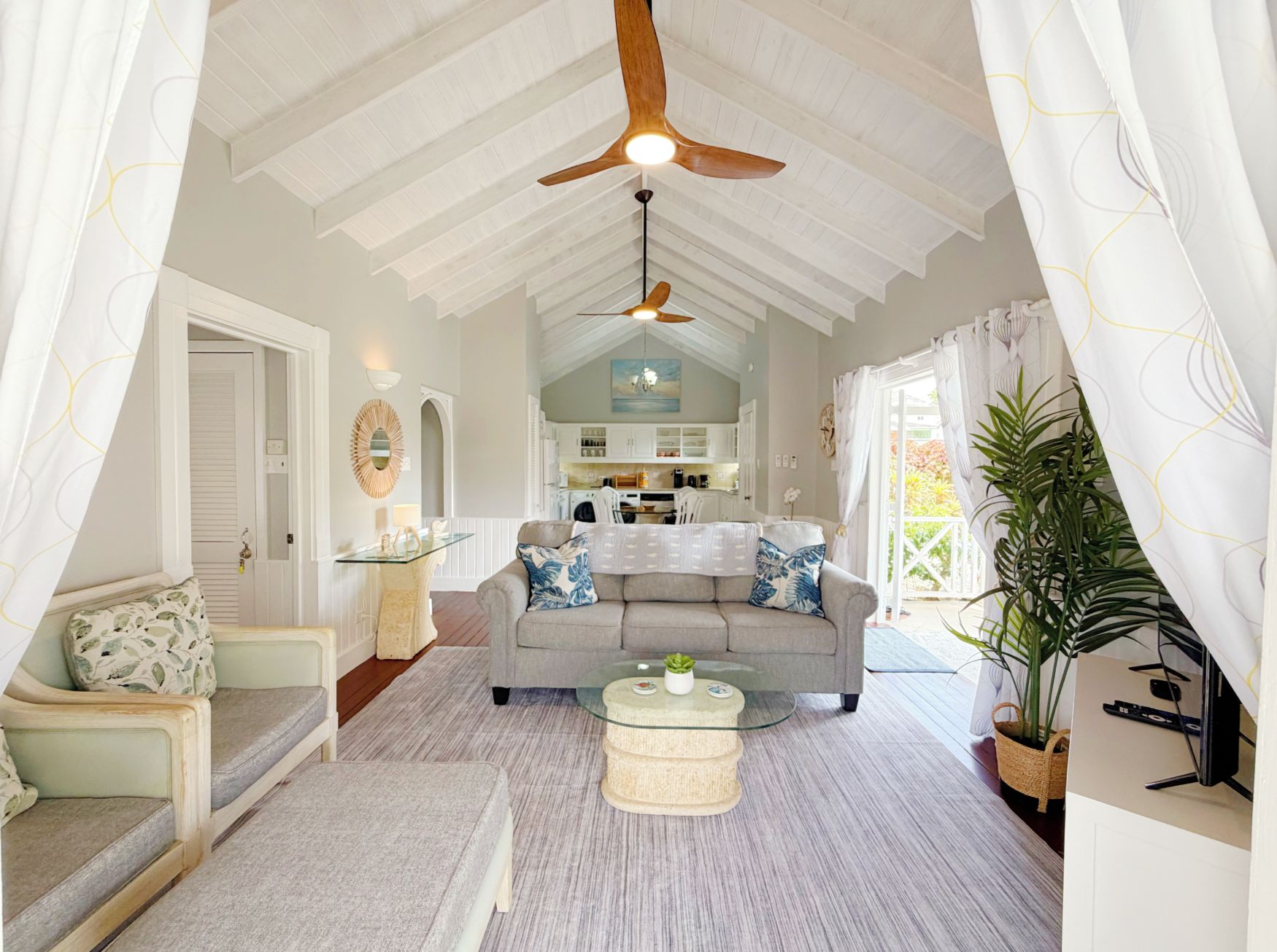 A spacious living room with a high ceiling fan, a glass coffee table, and a grey sofa.
