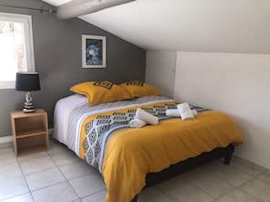 Um quarto com uma cama, duas almofadas, uma mesa de cabeceira com abajur e um quadro na parede.