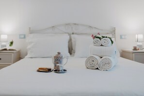 A neatly made bed with rolled towels, a teapot, and a tray with toast and tea.