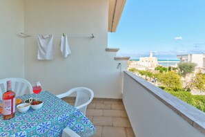 A balcony with a table set for two, a bottle of red wine, and a bowl of nuts.
