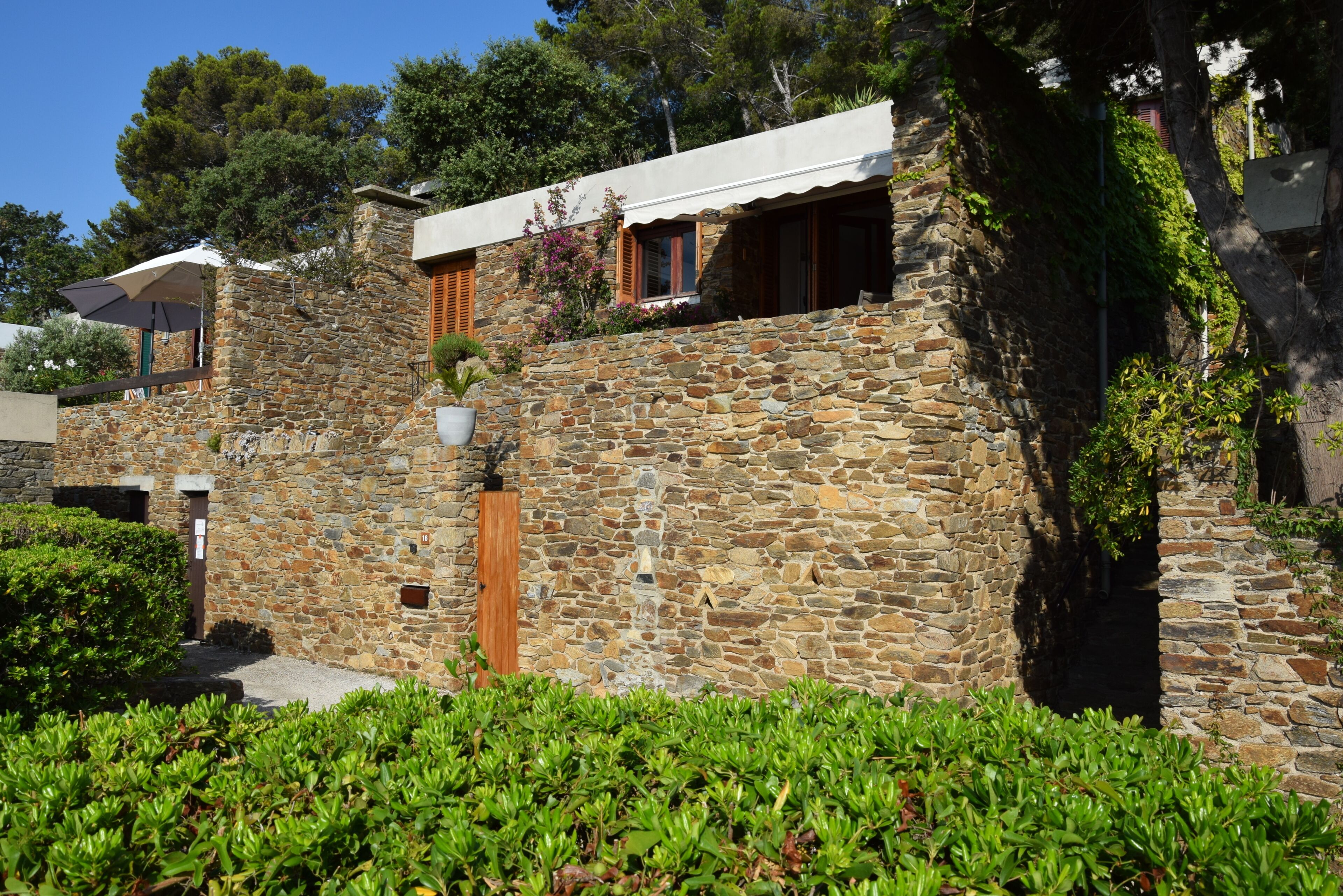 Un bâtiment en pierre avec une porte et des fenêtres en bois, entouré de verdure.
