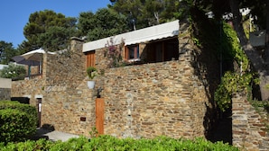Un edificio de piedra con puerta y ventanas de madera, rodeado de vegetación.