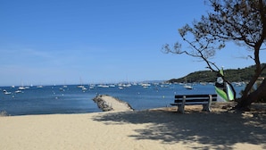 Una playa arenosa con un banco y un velero.