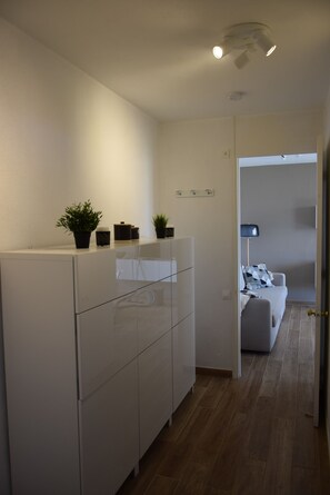 A modern kitchen with white cabinets, a countertop with potted plants, and a view into a living area with a sofa and a lamp.