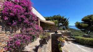 Un edificio de piedra con flores rosadas, un sendero de piedra y vista al mar.