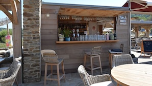 Zona de bar al aire libre con sillas de mimbre y un pilar de piedra.