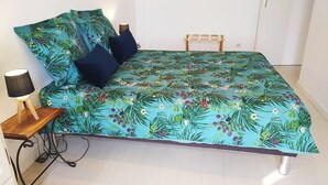 A bed with a floral bedspread, two dark pillows, a bedside table with a lamp, and a wooden chair. - DETACHED APARTMENT IN ANNECY'S HISTORICAL CENTER WITH PRIVATE GARDEN (Annecy)