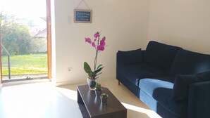 A living room with a dark blue sofa, a glass coffee table with plants, and a view of a garden through a glass door. - DETACHED APARTMENT IN ANNECY'S HISTORICAL CENTER WITH PRIVATE GARDEN (Annecy)