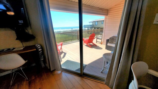 Una habitación con puerta de vidrio corredera que da a una terraza al aire libre con una silla roja y una mesa.