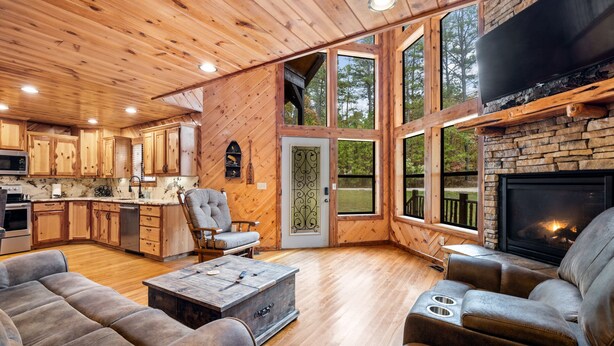 A spacious living area with a fireplace, wooden flooring, and large windows offering views of the outdoors. - Honey Hole Cabin is located on the Carson Creek Rd. Minutes to the Lake (Broken Bow)