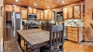 A wooden cabin-style kitchen with a central island, stainless steel appliances, and a large dining table. - Honey Hole Cabin is located on the Carson Creek Rd. Minutes to the Lake (Broken Bow)