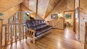 A log cabin interior with a leather sofa, wooden flooring, and a lofted sleeping area. - Honey Hole Cabin is located on the Carson Creek Rd. Minutes to the Lake (Broken Bow)