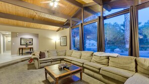 A spacious living room with a large sectional sofa, a wooden coffee table, and a ceiling fan. Large windows offer a view of the outdoors. - ***3200 Sq Ft 5 Bed 4 Bath 1 Story Private Pool/Spa W/ Casita (Las Vegas)