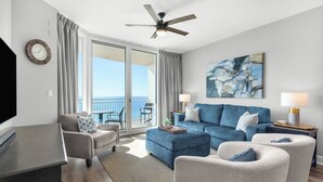 A modern living room with a sofa, armchairs, a TV, and a ceiling fan.