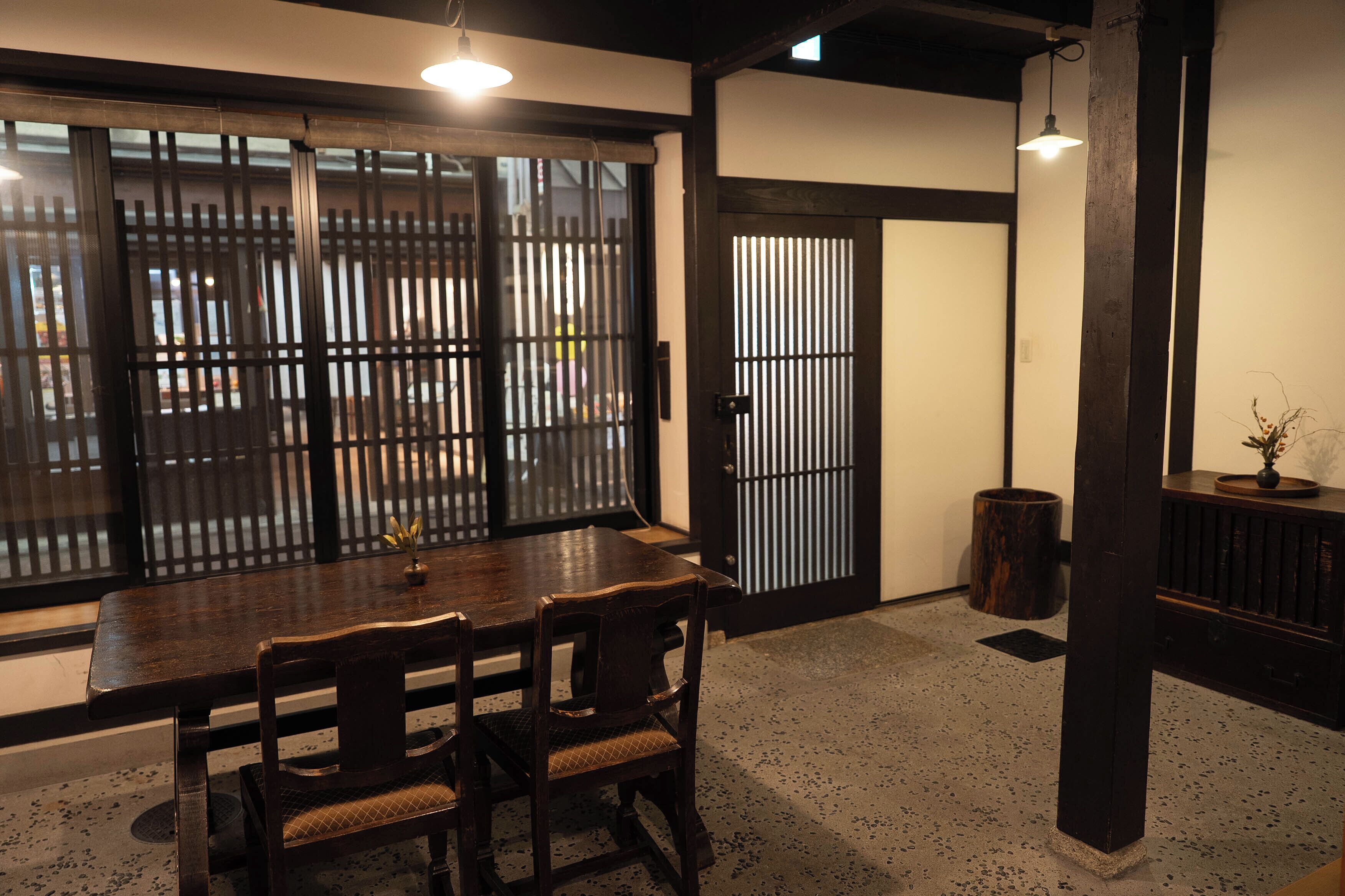 A traditional Japanese room with tatami flooring, a wooden dining table with chairs, a sliding door, and a small potted plant.