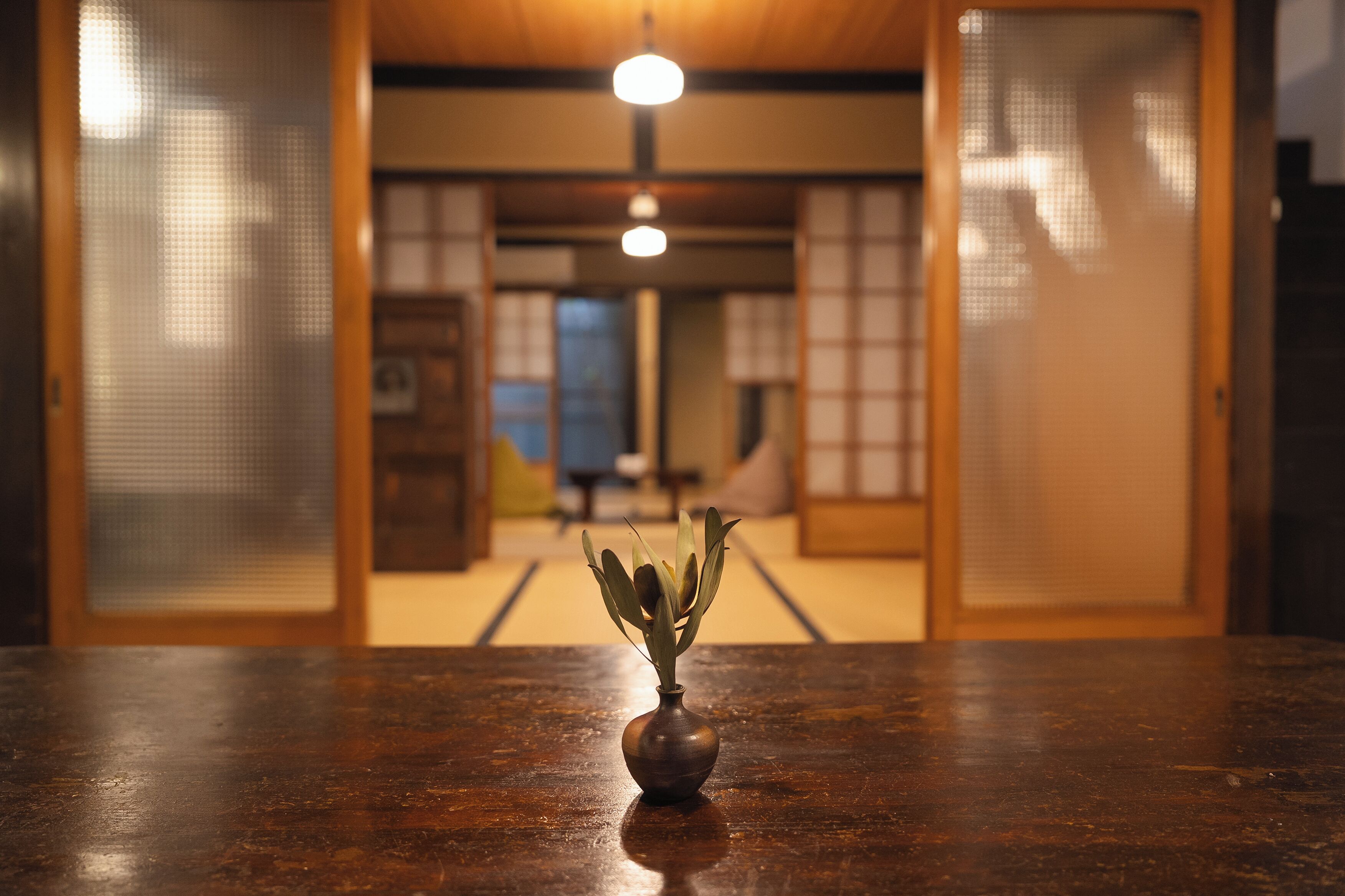 A traditional Japanese room with tatami flooring, a wooden table with a vase, and sliding doors.