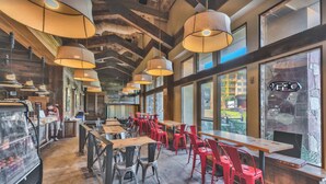 A restaurant interior with long wooden tables, red chairs, hanging pendant lights, and large windows offering views of the outside. - SUNDIAL LODGE PC~ PERFECT MT VILLAGE VIEW~ 5 STAR BY GUEST ~ PREMIUM  LOCATION! (Park City)