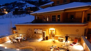 A heated outdoor pool area with lounge chairs and a hot tub, surrounded by a stone wall and a wooden deck. - SUNDIAL LODGE PC~ PERFECT MT VILLAGE VIEW~ 5 STAR BY GUEST ~ PREMIUM  LOCATION! (Park City)