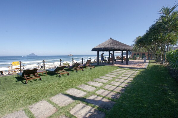 A beachside lounge area with sun loungers, a thatched-roof gazebo, and a view of the ocean.