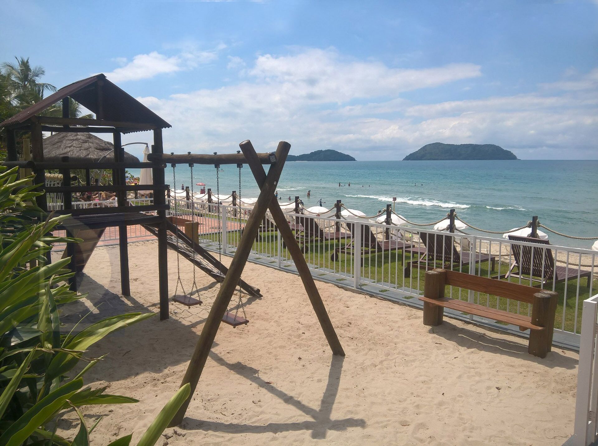 A beach with a swing set, a wooden structure, and umbrellas.
