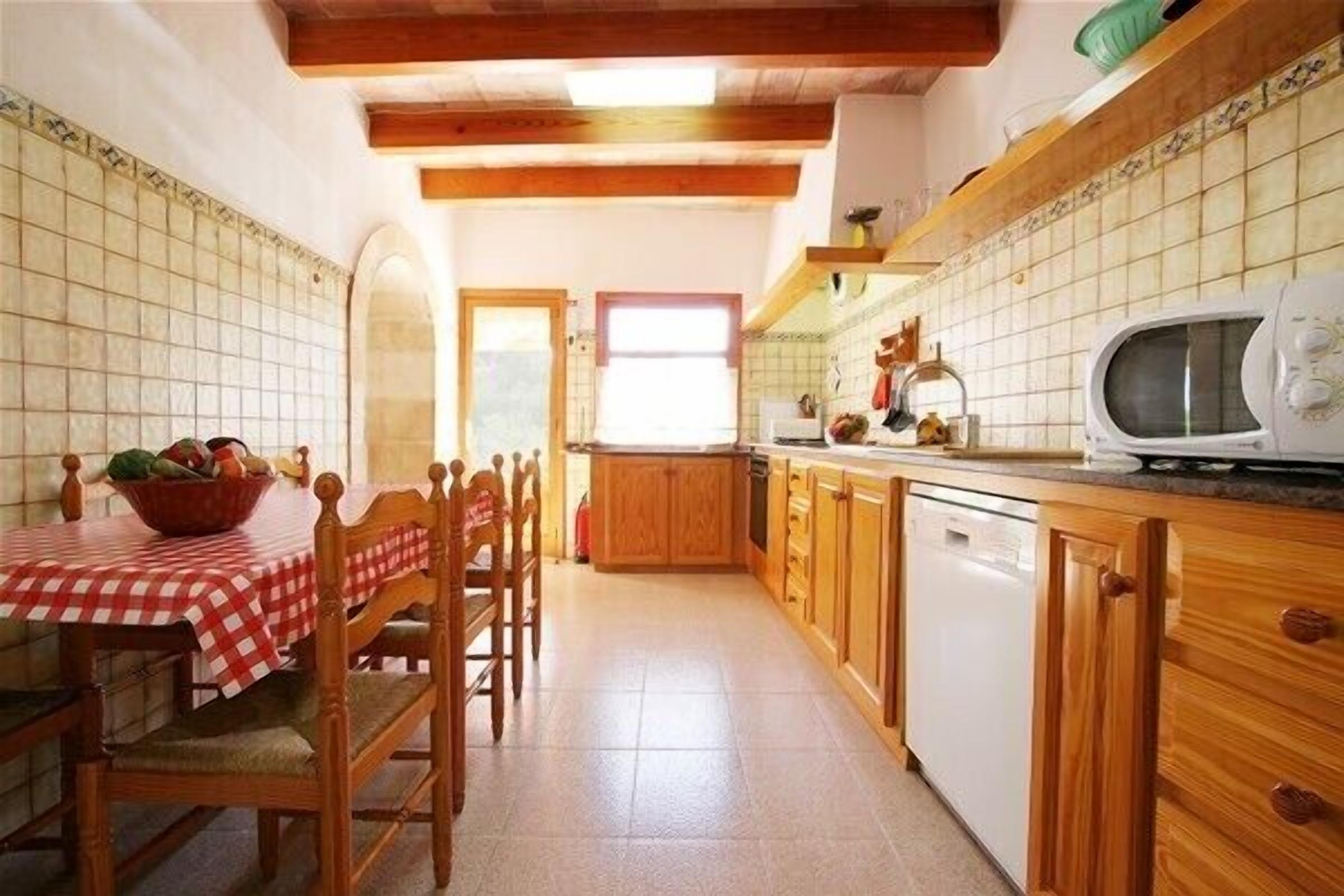 A kitchen with wooden cabinets, a white dishwasher, a microwave, and a table with a red and white checkered tablecloth.