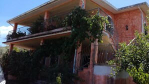 Ein zweigeschossiges Haus mit Balkon im oberen Geschoss, umgeben von viel Grün.