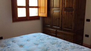 Ein Schlafzimmer mit einem Bett, einem Holzschrank und einem Fenster mit geöffnetem Vorhang.