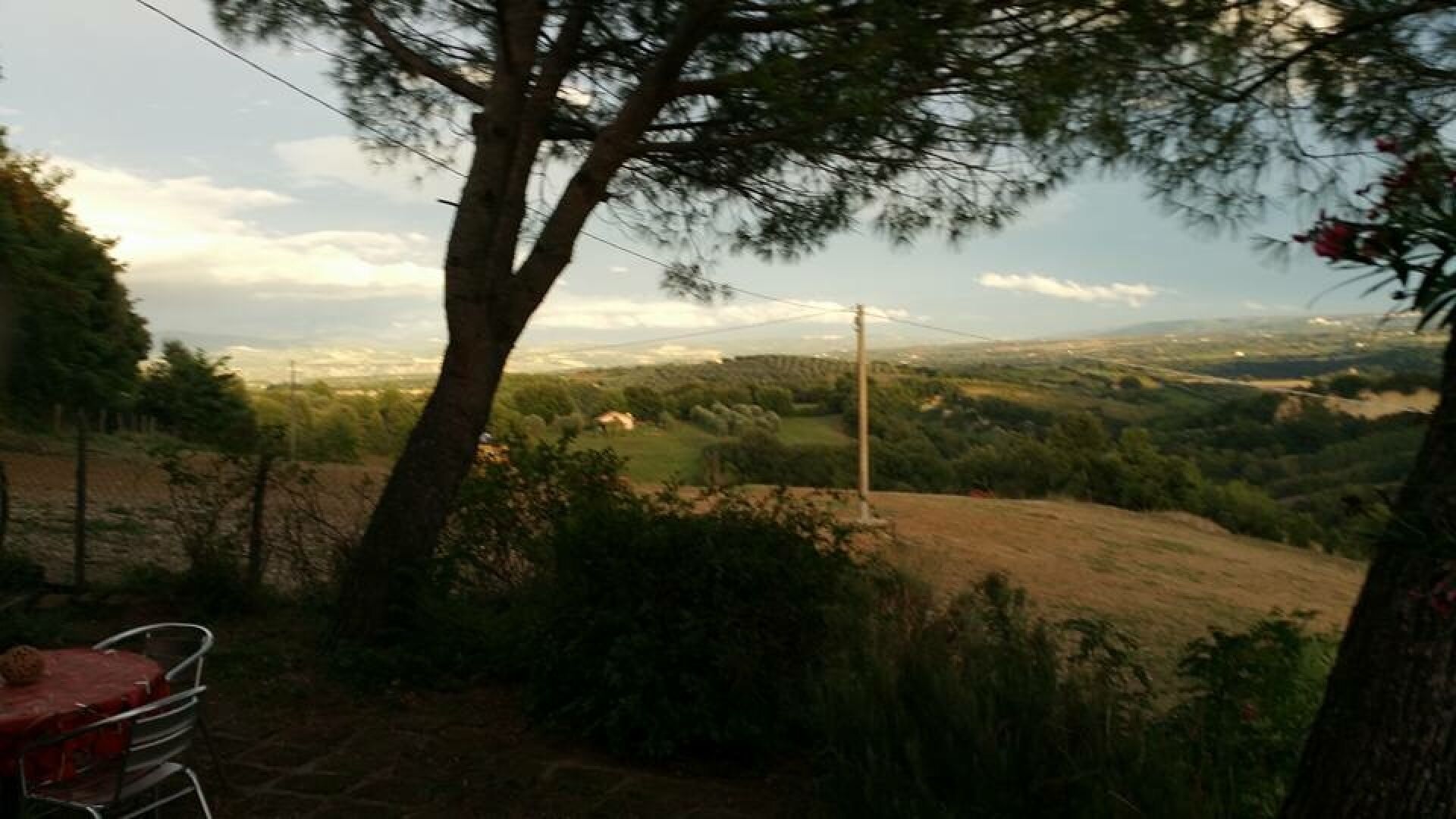 Ländliche Landschaft mit Baum, Stuhl und Blick auf ferne Hügel und Felder.