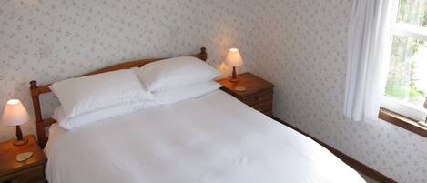 En snyggt bäddad säng med vita sängkläder, två sänglampor och ett blommigt tapetmönster.