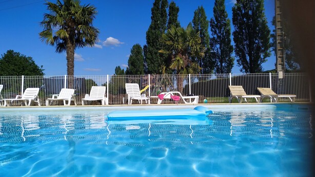 Une piscine à l’eau d’un bleu cristallin, entourée de chaises longues blanches et d’une clôture blanche.