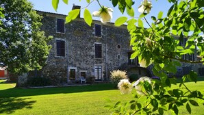 Un bâtiment en pierre, avec une pelouse verdoyante et des fleurs blanches au premier plan.
