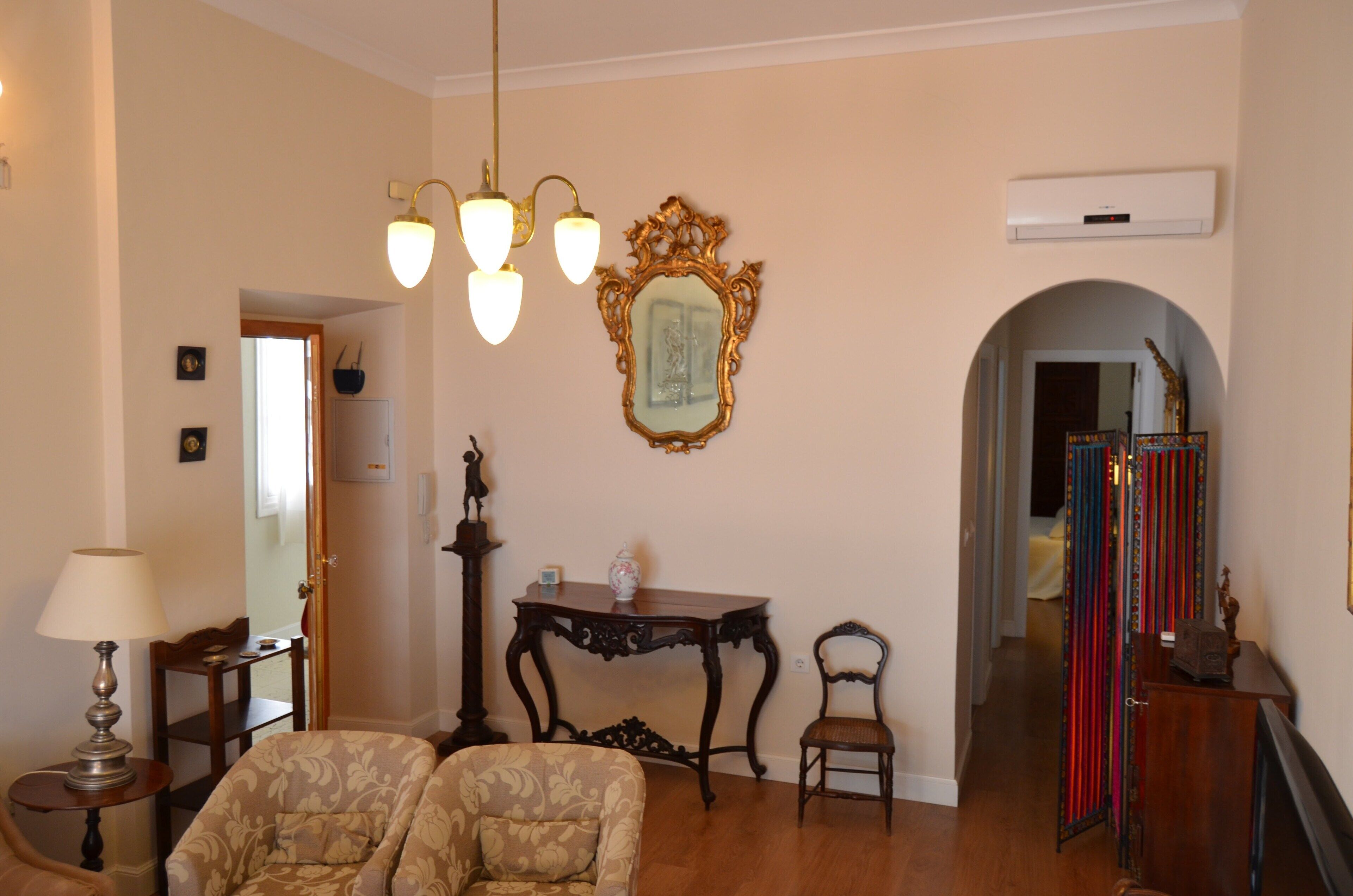 Een woonkamer met twee gestoffeerde fauteuils, een houten salontafel, een wandspiegel en een kroonluchter.